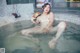 A naked woman sitting in a hot tub holding a hat.