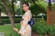 A woman in a kimono holding a fan in a park.