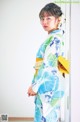 A woman in a blue and green kimono standing in front of a door.