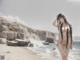 A nude woman standing on a beach next to the ocean.