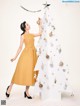 A woman in a yellow dress standing next to a white Christmas tree.