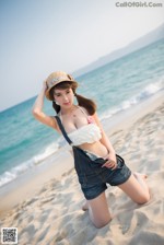 A woman in a straw hat is posing on the beach.