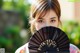 A woman holding a black fan in front of her face.