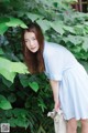 A woman in a blue and white striped dress leaning against a tree.