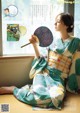 A woman in a kimono sitting on a window sill holding a fan.