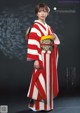 A woman in a red and white kimono standing in front of a black background.